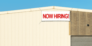 now hiring banner hanging on the outside of a warehouse